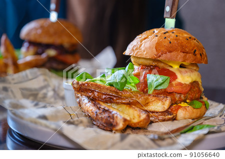 Two delicious juicy beef, cheese and vegetable burgers on a table in a cafe. Big burger, american fast food. 91056640