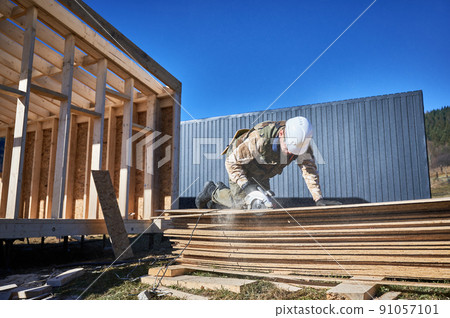 Carpenter using circular saw for cutting wooden OSB board. Man worker building wooden frame house on pile foundation. Carpentry concept. 91057101