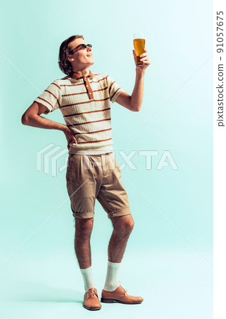 Potrait of young man in casual outfit drinkig cool beer, posing isolated over light blue studio background Potrait of young man in casual outfit drinkig cool beer, posing isolated over light blue studio background 91057675