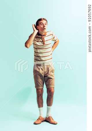 Full-length portrait of young man in retro style outfit posing isolated over light blue studio background. Overhearing Full-length portrait of young man in retro style outfit posing isolated over light blue studio background. Overhearing 91057692