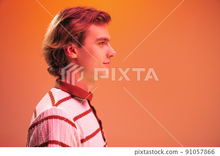 Side view portrait of young handsome man posing, looking away isolated over orange studio background in neon light Side view portrait of young handsome man posing, looking away isolated over orange studio background in neon light 91057866