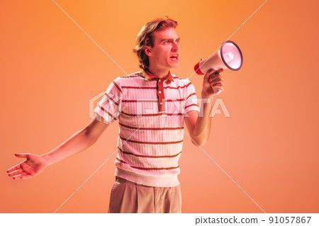 Portrait of young man shouting in megaphone isolated over orange studio background in neon light. Emotive, active speech Portrait of young man shouting in megaphone isolated over orange studio background in neon light. Emotive, active speech 91057867