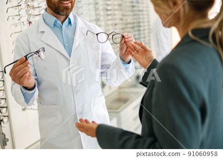 Close up of male optician showing glasses to woman at optics store 91060958