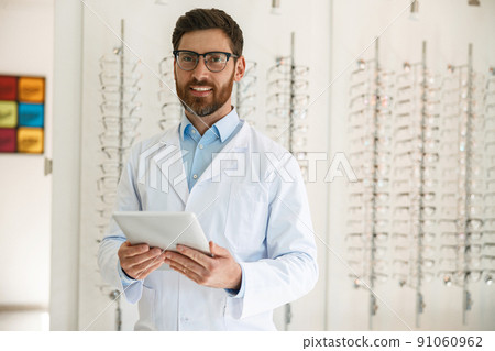 Handsome ophthalmologist with digital tablet in front of the showcase with eyeglasses Handsome ophthalmologist with digital tablet in front of the showcase with eyeglasses 91060962