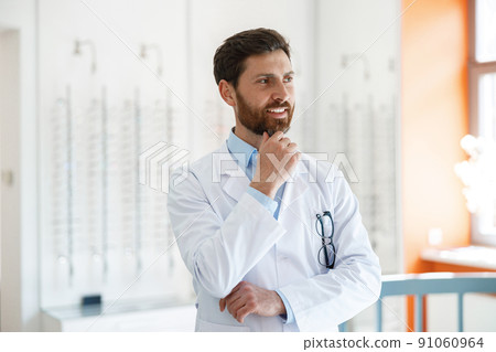 Portrait of smiling ophthalmologist in front of showcase in optics store looks away Portrait of smiling ophthalmologist in front of showcase in optics store looks away 91060964