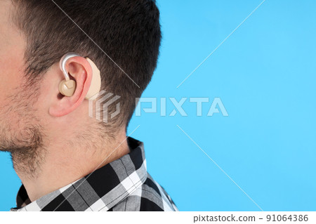 Young man with hearing aid on blue background 91064386