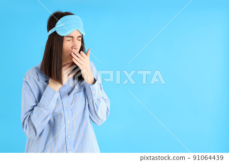 Attractive woman in sleep mask on blue background Attractive woman in sleep mask on blue background 91064439