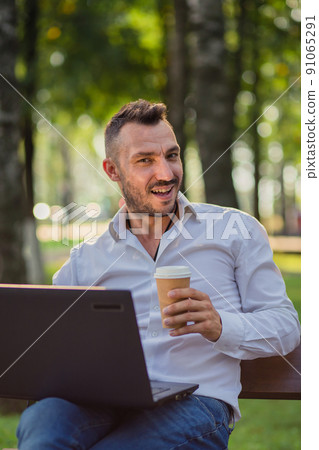 Laughing businessman is working in the park with a laptop, drinking coffee. 91065291