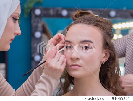 Make-up artist with a brush paints the eyelid close-up of a girl in the salon. Make-up artist with a brush paints the eyelid close-up of a girl in the salon. 91065295