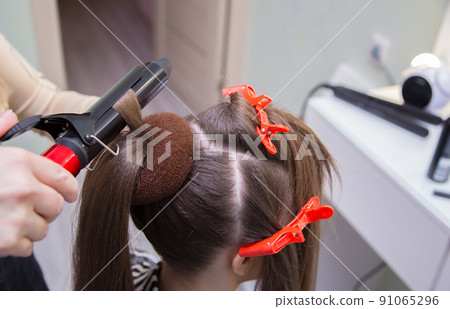 Close-up of a hand curling a strand of hair on a woman's head with tongs. Close-up of a hand curling a strand of hair on a woman's head with tongs. 91065296