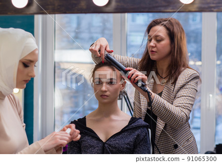 Two women professionally curl hair and make up a girl in a salon. Two women professionally curl hair and make up a girl in a salon. 91065300
