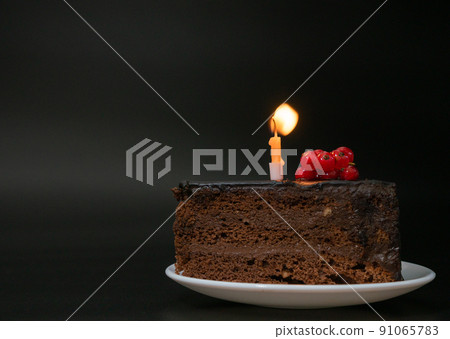 Piece of chocolate birthday cake with one burning candle on white plate on deep black background. Birthday party, celebration, anniversary. Close-up, copy space for your text. Piece of chocolate birthday cake with one burning candle on white plate on deep black background. Birthday party, celebration, anniversary. Close-up, copy space for your text. 91065783