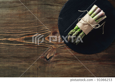 An edible, raw stems of asparagus on a wooden background. 91066253