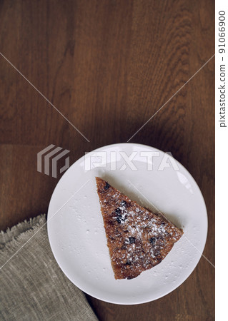 Part of the pie is on a white plate on the table. A piece of lemongrass with blueberries and cranberries without milk and eggs on flaxseed flour. The concept of healthy eating. High quality photo 91066900