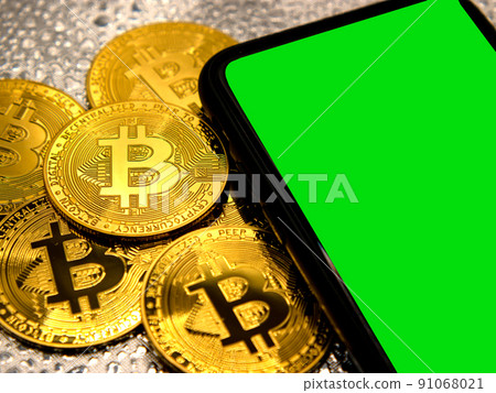 Bitcoin coins in golden metal with a smarthphone beside it, green screen area copy space 91068021