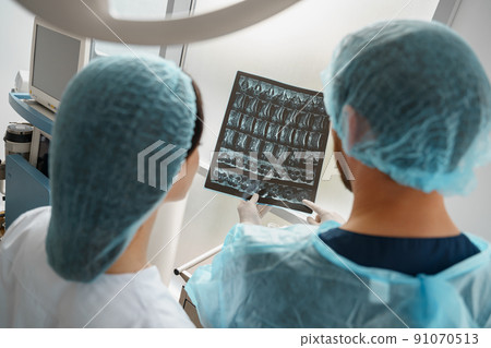Doctor and nurse in uniform look and discuss an X-ray or MRI scan of the patient spine 91070513