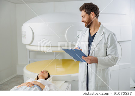 Radiologist controls MRI or CT or PET Scan with female patient undergoing procedure 91070527