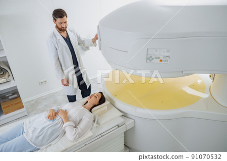 Radiologist controls MRI or CT or PET Scan with female patient undergoing procedure Radiologist controls MRI or CT or PET Scan with female patient undergoing procedure 91070532