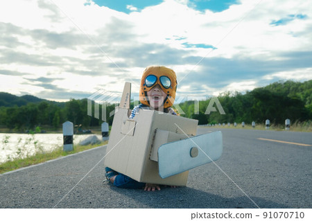Cute dreamer little girl playing with cardboard planes on a lake road on a sunny day. Happy kid playing with cardboard plane against blue summer sky background. Childhood dream imagination concept. 91070710