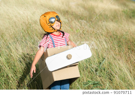 Cute dreamer little girl playing with cardboard planes in the meadow on a sunny day. Happy kid playing with cardboard plane against blue summer sky background. Childhood dream imagination concept. 91070711