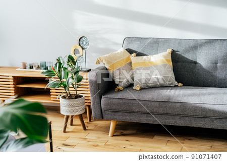 Stylish living room interior with designer console with decor and gray sofa with graphic pillows. White walls, green plants in the pots. Light wooden oak parquet. Modern Scandinavian style interior. 91071407