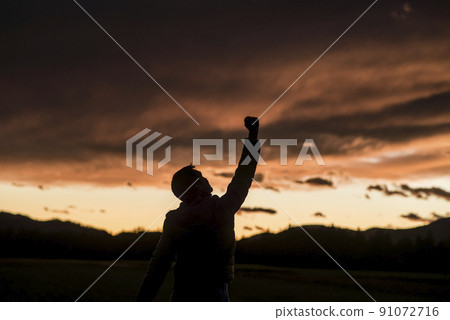 Jubilant man raising his fist against a sunset 91072716