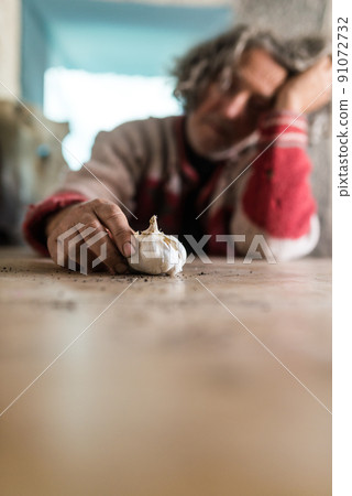 Man with dirty hands holding a bulb of garlic as he sits at table 91072732