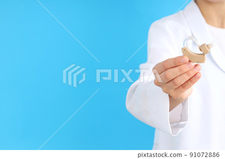 Doctor holding a hearing aid on a blue background Doctor holding a hearing aid on a blue background 91072886