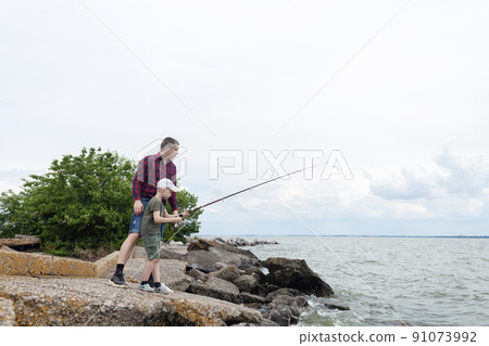 Father and son fishing. Dad shows his son how to hold the spinning and spin the reel. Fishing training on a pond or river. Caring parent concept. 91073992
