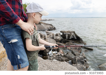 Father and son fishing. Dad shows his son how to hold the spinning and spin the reel. Fishing training on a pond or river. Caring parent concept. 91073993