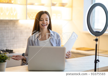 Woman with papers smiling at laptop Woman with papers smiling at laptop 91075583