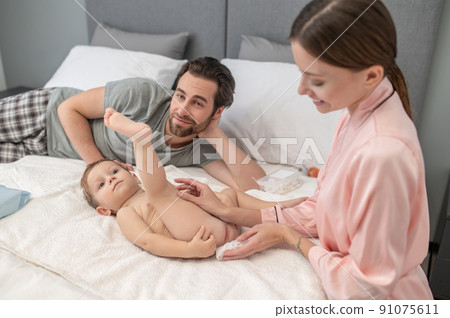 Woman touching powder on babys skin and dad watching 91075611