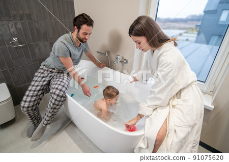 Young parents sitting on bathtub bathing baby 91075620