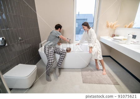 Man and woman crouching on bathtub bathing child Man and woman crouching on bathtub bathing child 91075621