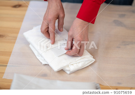 Top view of hands putting card into folded shirt 91075659