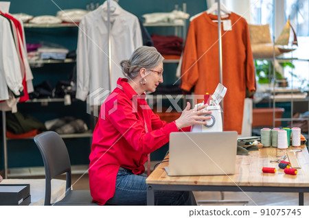 Woman touching sewing machine sitting sideways to camera Woman touching sewing machine sitting sideways to camera 91075745