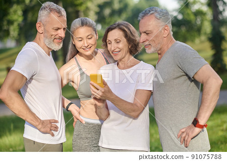 A group of people looking at the photos in a smartphone 91075788