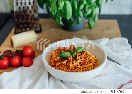 Served plate of just cooked homemade fettuccine pasta with creamy tomato sauce, seafood and parmesan cheese, decorated with basil leaves on the kitchen table. Selective focus Served plate of just cooked homemade fettuccine pasta with creamy tomato sauce, seafood and parmesan cheese, decorated with basil leaves on the kitchen table. Selective focus 91076003