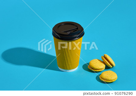 Hot coffee in yellow paper cup with black lid and macaroons on b Hot coffee in yellow paper cup with black lid and macaroons on b 91076290