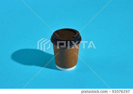 Hot coffee in brown paper cup with black lid on blue background Hot coffee in brown paper cup with black lid on blue background 91076297