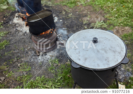 Hiking pot, Bowler in the bonfire. in cauldron at the stake. Traveling, tourism, picnic cooking, cooking at the stake in a cauldron, fire and smoke. Hiking pot, Bowler in the bonfire. in cauldron at the stake. Traveling, tourism, picnic cooking, cooking at the stake in a cauldron, fire and smoke. 91077216