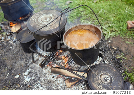 Hiking pot, Bowler in the bonfire. in cauldron at the stake. Traveling, tourism, picnic cooking, cooking at the stake in a cauldron, fire and smoke. Hiking pot, Bowler in the bonfire. in cauldron at the stake. Traveling, tourism, picnic cooking, cooking at the stake in a cauldron, fire and smoke. 91077218