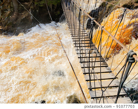 Above the fountain with yellow-brown water and protruding stones there is a rope wooden ladder. High quality photo 91077703