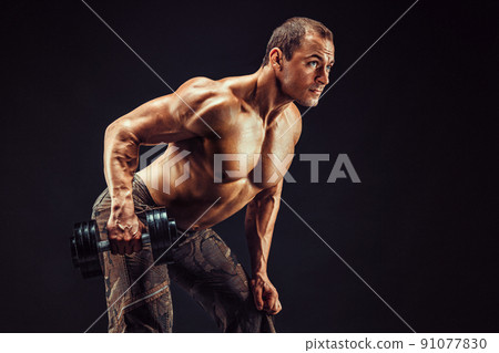 Powerful man doing the exercises with dumbbells. Photo of young man with good physique isolated on black background. Powerful man doing the exercises with dumbbells. Photo of young man with good physique isolated on black background. 91077830