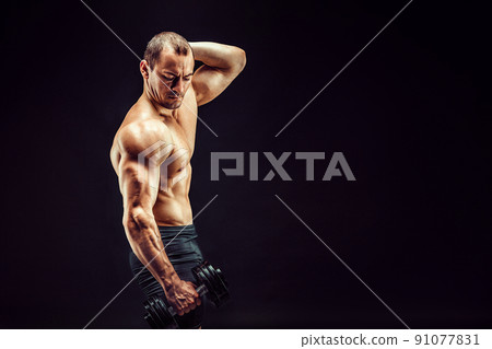 Powerful man doing the exercises with dumbbells. Photo of young man with good physique isolated on black background. Powerful man doing the exercises with dumbbells. Photo of young man with good physique isolated on black background. 91077831