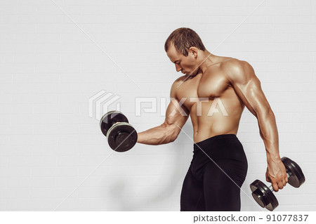 Powerful man doing the exercises with dumbbells. Photo of young man with good physique isolated on white background. Strength and motivation 91077837
