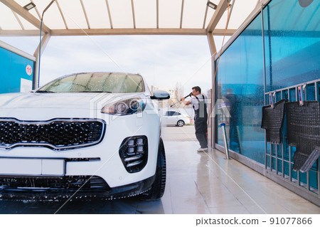self-service car wash. a man in a work jumpsuit washes the car from a hose. self-service car wash. a man in a work jumpsuit washes the car from a hose. 91077866