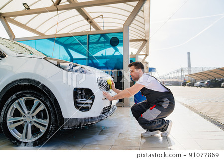 self-service car wash. a man in a work jumpsuit washes the car with a sponge  91077869
