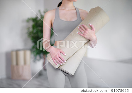Young woman holding yoga mats while standing in a light studio. Young woman holding yoga mats while standing in a light studio. 91078635