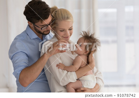 Baby in diaper on parents arms drinks water from bottle Baby in diaper on parents arms drinks water from bottle 91078742